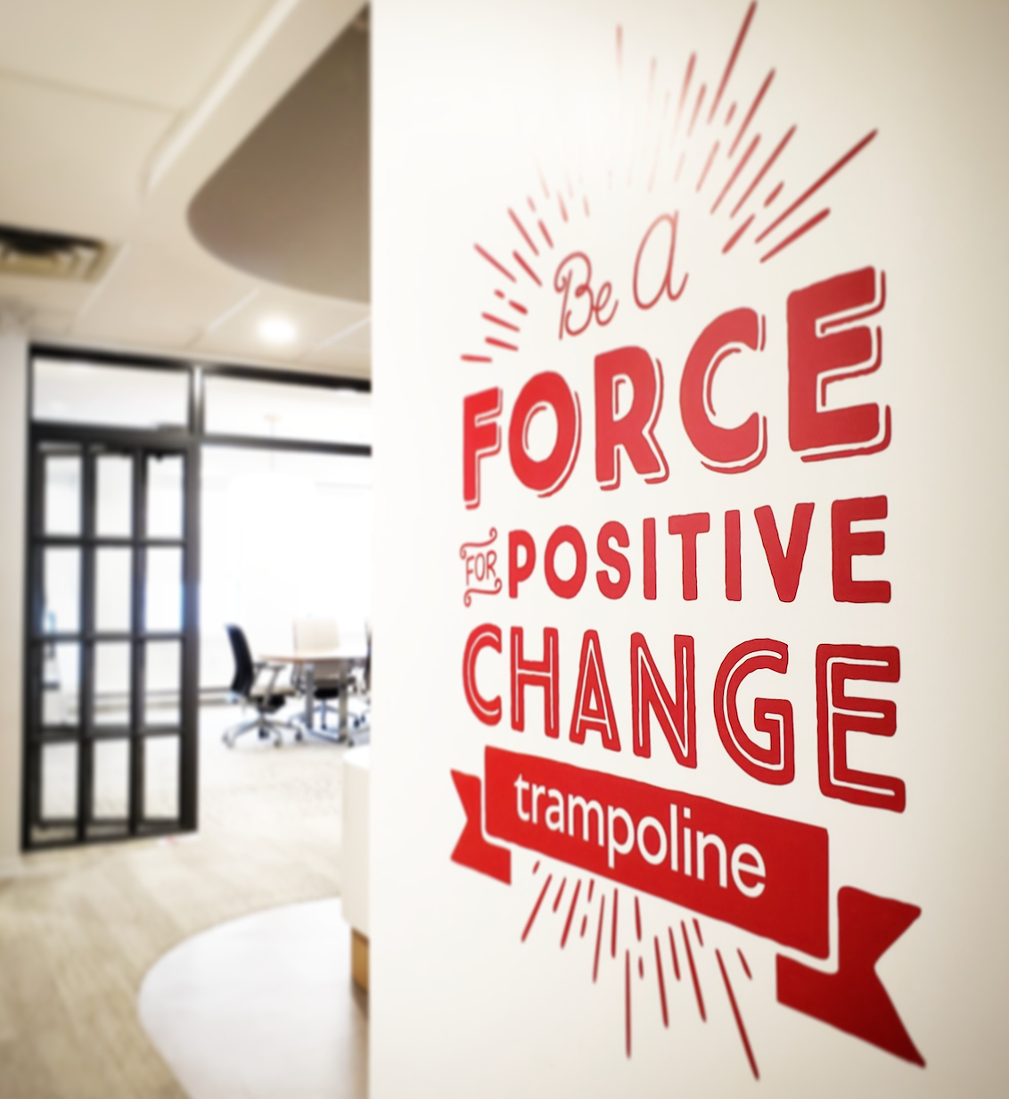 Wall decal with red text "Be a Force for Positive Change" placed beside Trampoline boardroom