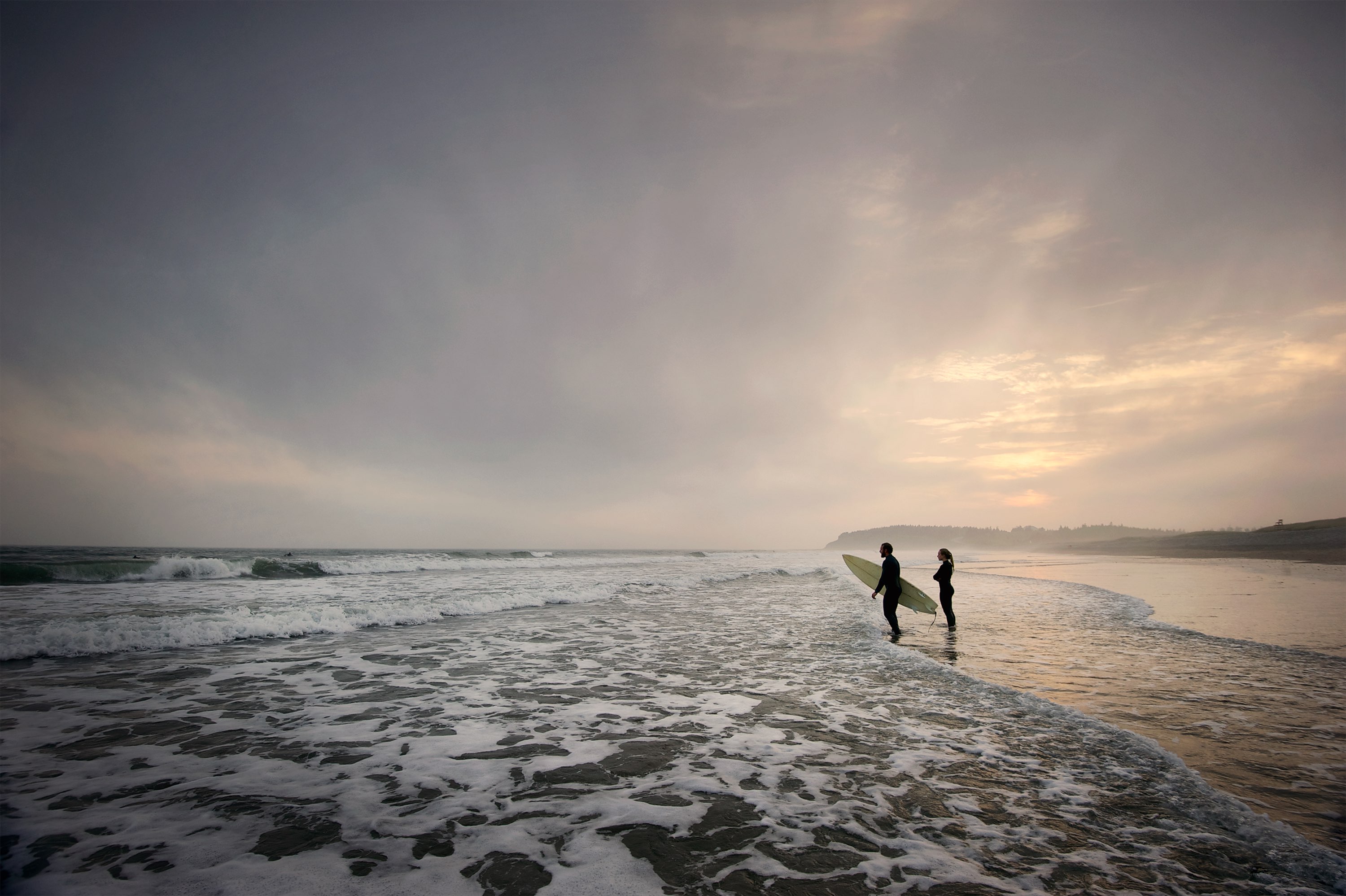 Two surfers standing in the waves of a beach on the shore